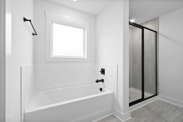 full bathroom featuring a shower stall, a garden tub, baseboards, and wood finished floors