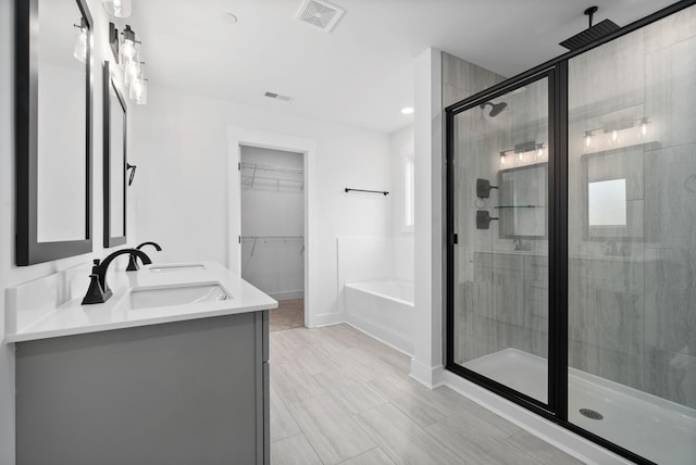bathroom featuring a shower stall, a garden tub, a walk in closet, double vanity, and baseboards
