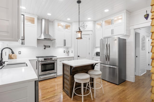 kitchen featuring stainless steel appliances, wall chimney exhaust hood, a sink, light wood-style flooring, and white cabinets