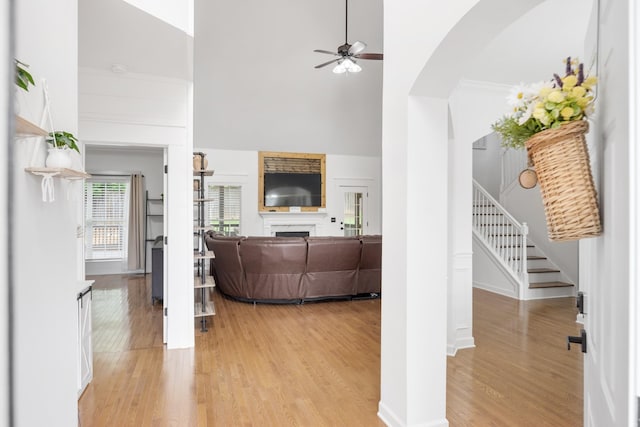 living area with a ceiling fan, light wood-style floors, stairway, a towering ceiling, and arched walkways