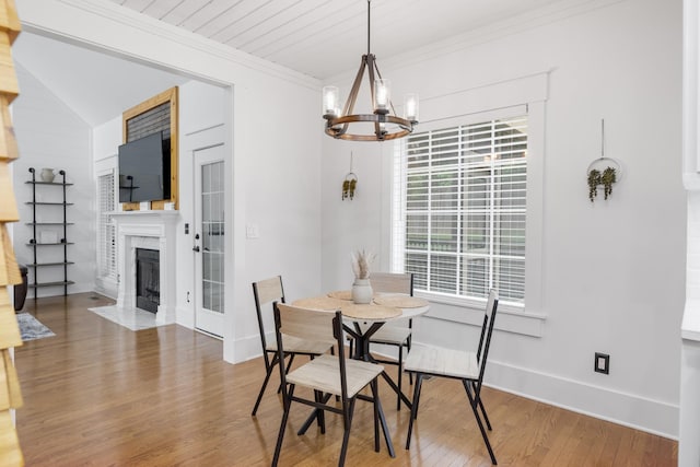 dining area with a chandelier, wood finished floors, crown molding, a fireplace with flush hearth, and baseboards