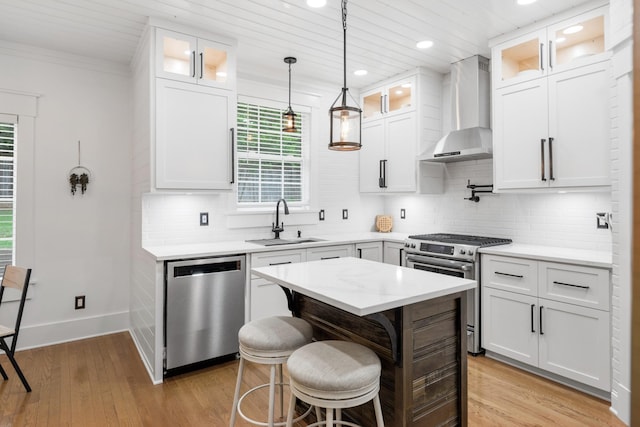 kitchen with stainless steel appliances, a sink, wall chimney range hood, a breakfast bar area, and white cabinets