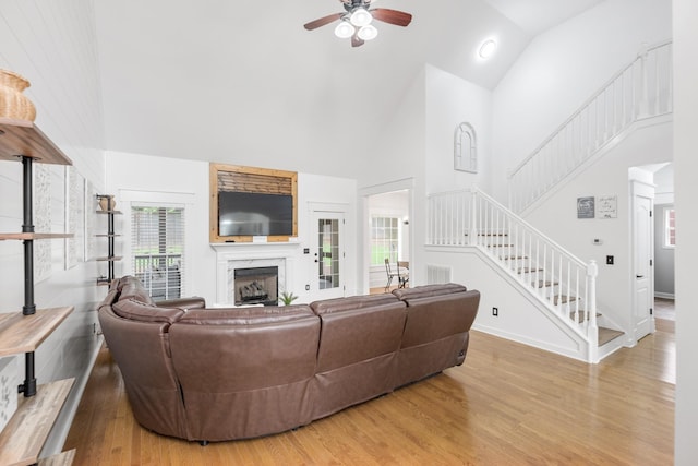 living area with high vaulted ceiling, ceiling fan, wood finished floors, stairs, and plenty of natural light