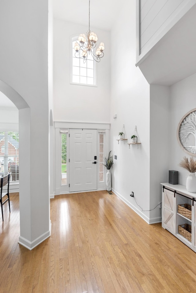 entryway with a towering ceiling, arched walkways, a chandelier, light wood finished floors, and plenty of natural light