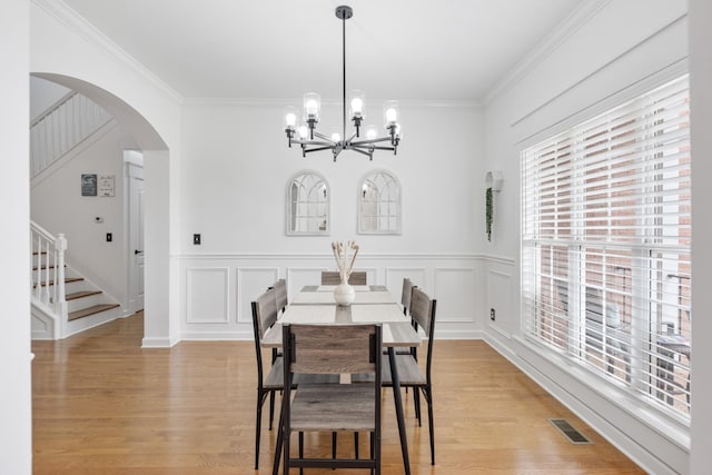 dining room featuring stairway, arched walkways, crown molding, a chandelier, and light wood-style floors