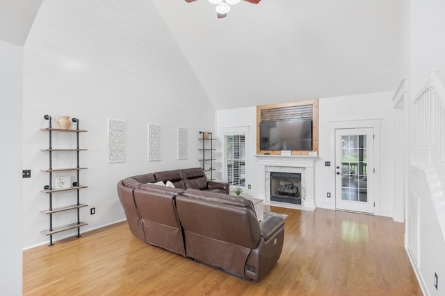 living room with high vaulted ceiling, a premium fireplace, a ceiling fan, light wood-style flooring, and plenty of natural light