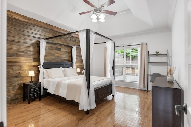 bedroom with a raised ceiling, ornamental molding, wooden walls, light wood-style flooring, and a ceiling fan