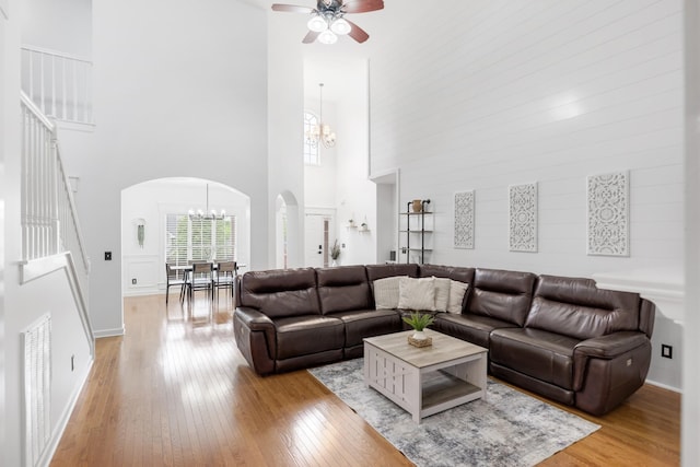 living area with a chandelier, a towering ceiling, arched walkways, light wood-style flooring, and ceiling fan