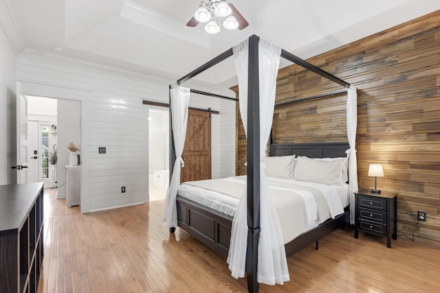 bedroom with wooden walls, ornamental molding, light wood-style floors, ensuite bath, and a barn door