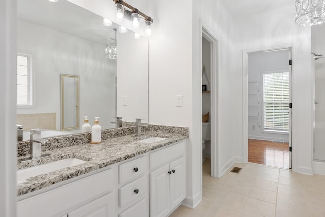 full bath featuring a chandelier, tile patterned flooring, double vanity, baseboards, and toilet