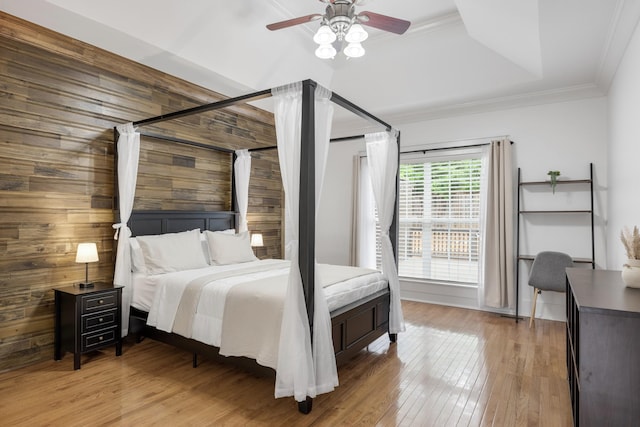 bedroom featuring light wood-type flooring, ornamental molding, wood walls, and a ceiling fan