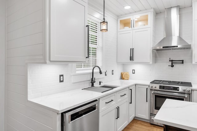 kitchen featuring wall chimney exhaust hood, appliances with stainless steel finishes, a sink, decorative backsplash, and white cabinetry
