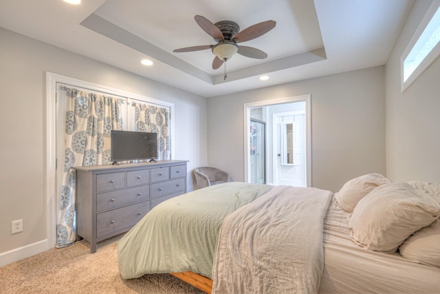bedroom featuring a tray ceiling, light colored carpet, recessed lighting, baseboards, and ensuite bathroom