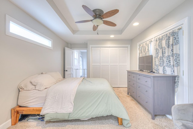 bedroom with a closet, a raised ceiling, recessed lighting, light carpet, and a ceiling fan