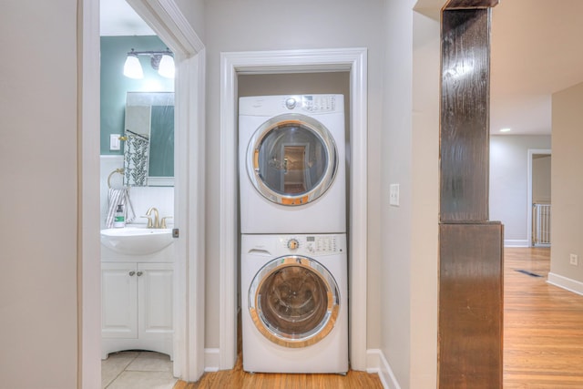 laundry room with stacked washer and clothes dryer, baseboards, and wood finished floors
