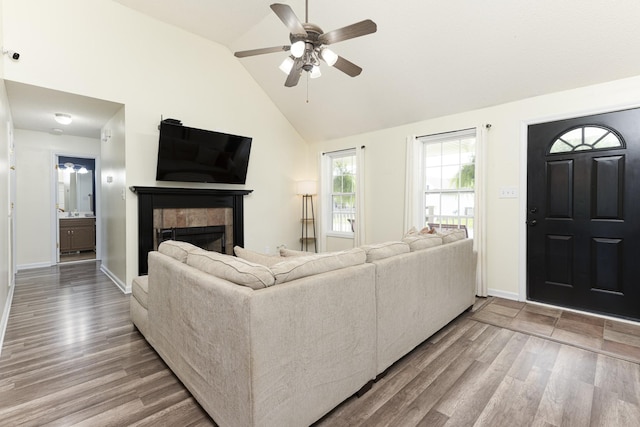 living area with wood finished floors, ceiling fan, a tile fireplace, lofted ceiling, and baseboards