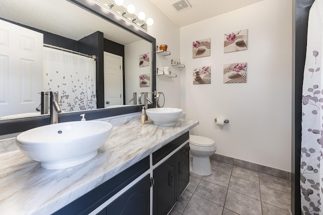 bathroom with double vanity, tile patterned floors, baseboards, toilet, and a textured ceiling