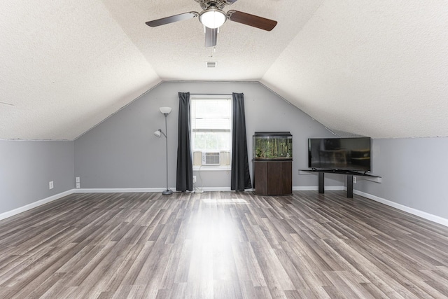 additional living space featuring a textured ceiling, vaulted ceiling, wood finished floors, a ceiling fan, and baseboards