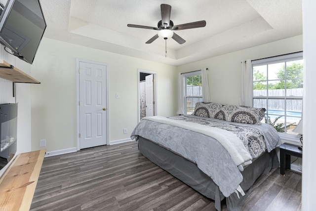 bedroom with a tray ceiling, dark wood-style flooring, baseboards, ceiling fan, and ensuite bathroom