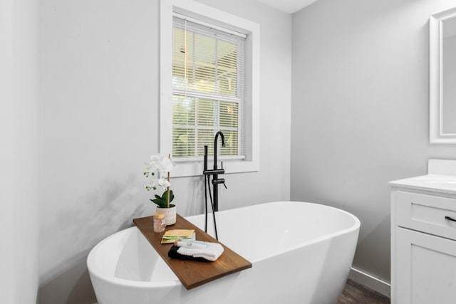 full bath featuring vanity, a freestanding tub, and baseboards