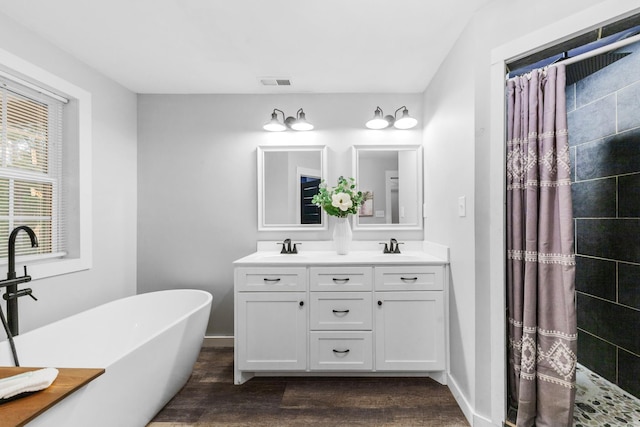 bathroom featuring wood finished floors, double vanity, a tile shower, and a freestanding tub