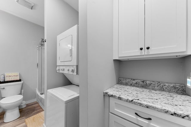 laundry area featuring stacked washer / dryer, wood finished floors, and baseboards