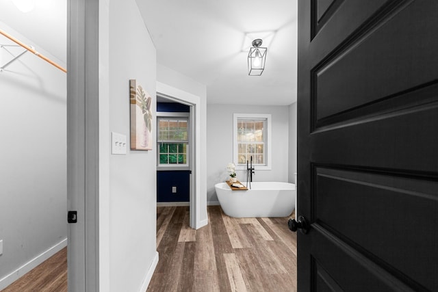 bathroom with wood finished floors, a soaking tub, and baseboards