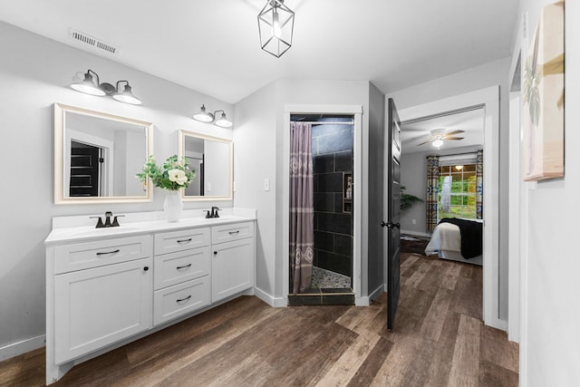 ensuite bathroom with wood finished floors, a tile shower, double vanity, and baseboards