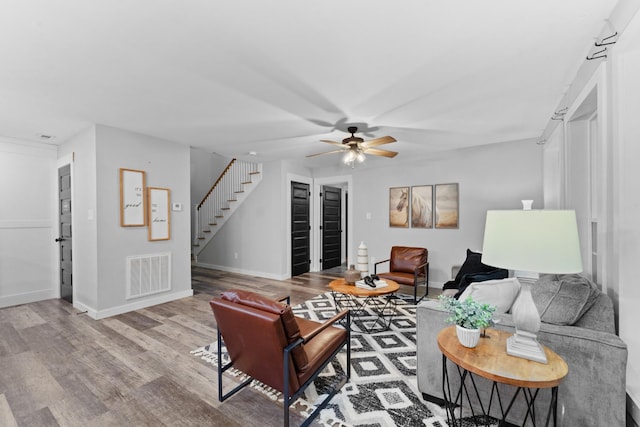 living area with stairs, wood finished floors, ceiling fan, and baseboards