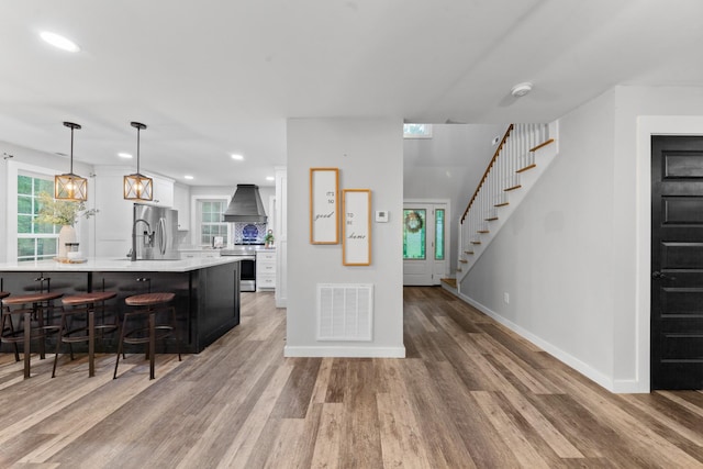 kitchen featuring stainless steel appliances, custom exhaust hood, light wood-type flooring, light countertops, and a breakfast bar area
