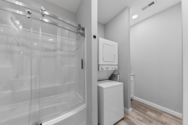 bathroom featuring stacked washing machine and dryer, a shower with door, wood finished floors, and baseboards
