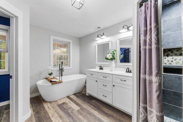 bathroom with wood finished floors, a freestanding tub, double vanity, and baseboards