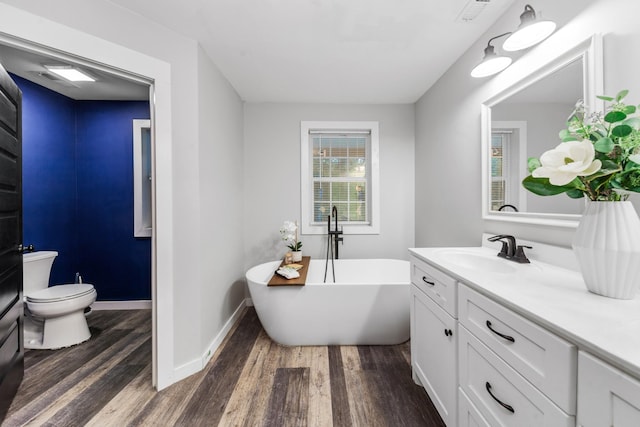 bathroom featuring wood finished floors, vanity, toilet, and a freestanding tub