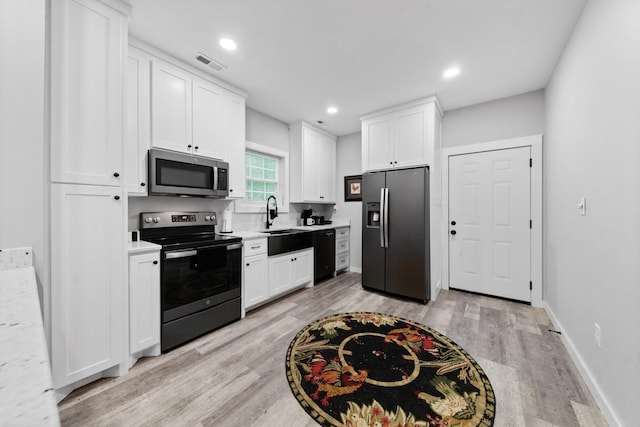 kitchen featuring appliances with stainless steel finishes, light countertops, a sink, light wood-type flooring, and white cabinets