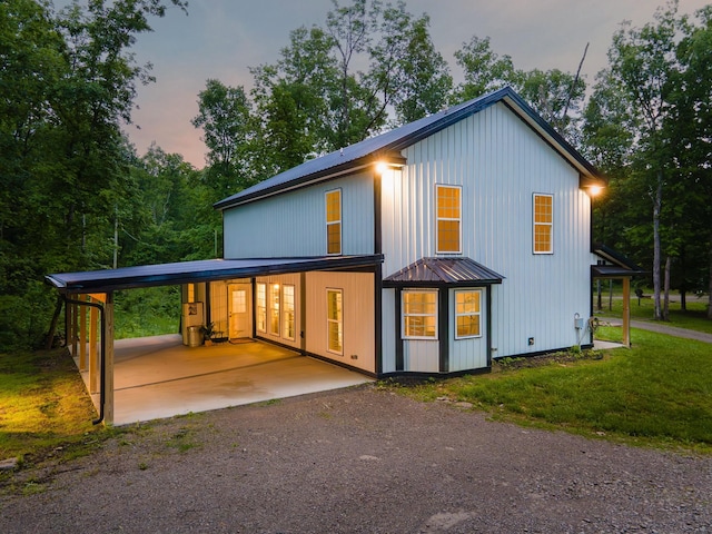 back of property featuring metal roof, an attached carport, a standing seam roof, a yard, and dirt driveway