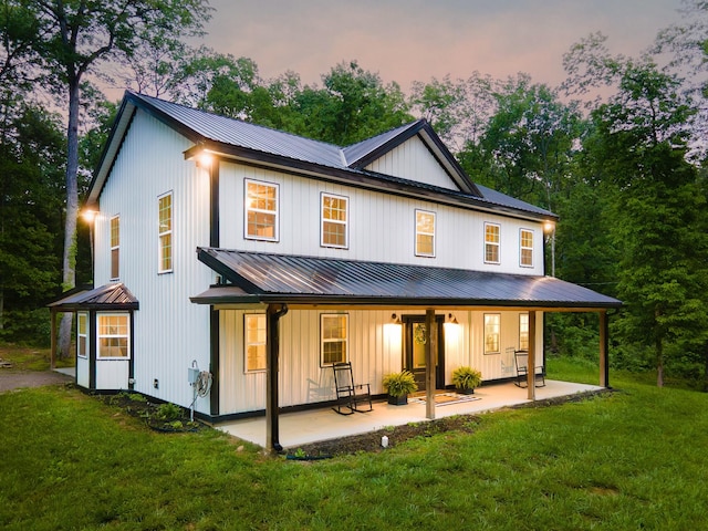 back of house at dusk featuring a lawn, a porch, metal roof, and board and batten siding