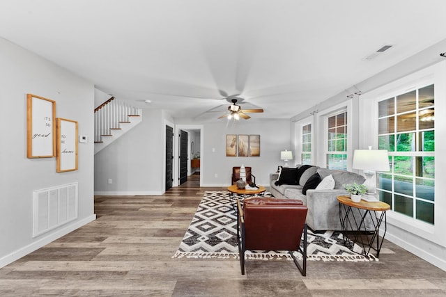living room with baseboards, wood finished floors, ceiling fan, and stairway