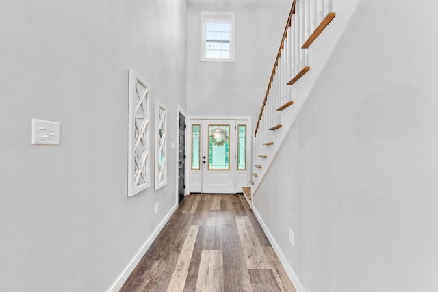 doorway to outside featuring wood finished floors, stairway, a high ceiling, and baseboards