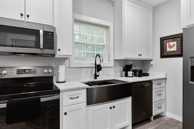 kitchen with stainless steel appliances, a sink, white cabinetry, and light wood finished floors