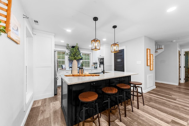 kitchen with freestanding refrigerator, white cabinetry, recessed lighting, light wood finished floors, and light stone countertops