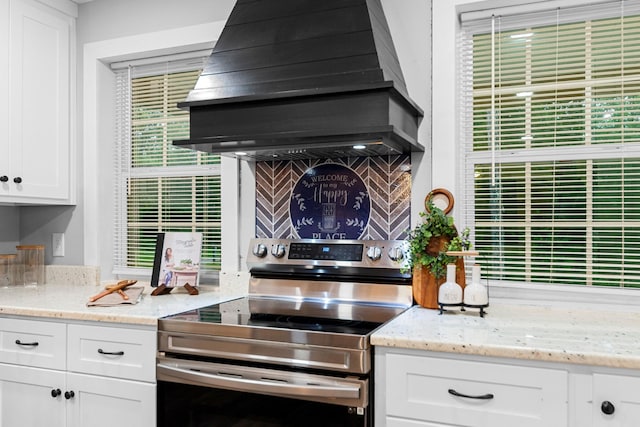 kitchen featuring electric stove, wall chimney exhaust hood, white cabinetry, and light stone countertops