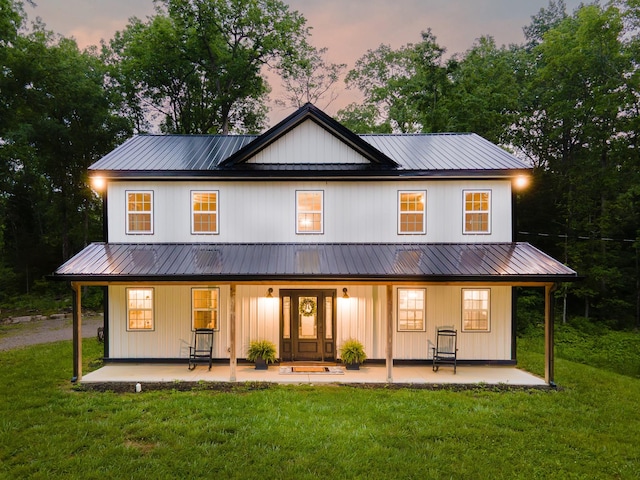 back of house at dusk featuring covered porch, a lawn, and metal roof