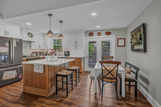 kitchen featuring stainless steel appliances, light countertops, backsplash, dark wood-style floors, and a breakfast bar area