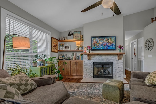 living area with ceiling fan, vaulted ceiling, wood finished floors, and a stone fireplace