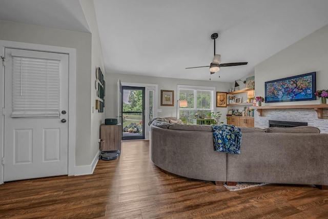 living room with a ceiling fan, a fireplace, dark wood-style floors, vaulted ceiling, and baseboards