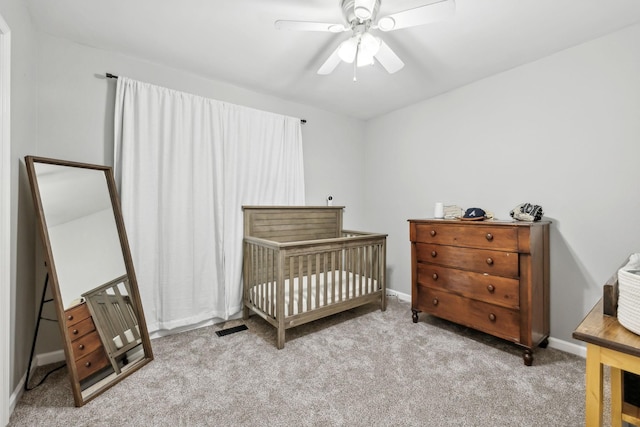carpeted bedroom featuring baseboards, a crib, and a ceiling fan