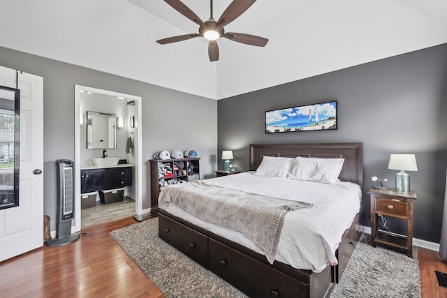 bedroom with wood finished floors, baseboards, vaulted ceiling, connected bathroom, and a sink