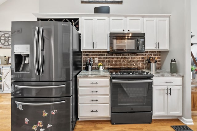 kitchen with black appliances, decorative backsplash, white cabinetry, light stone counters, and light wood finished floors