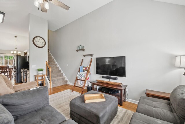 living area with vaulted ceiling, stairs, ceiling fan, a chandelier, and wood finished floors