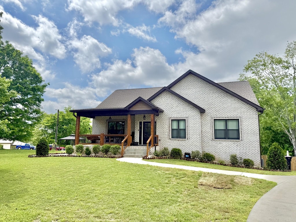 view of front of house with covered porch, a front lawn, brick siding, and a shingled roof